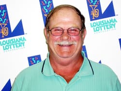 Mustached man in an aqua polo smiles in front of a white background patterned with the 飞艇168®幸运体彩预测-全国统一Louisiana在线官方查询结果网-最新体彩预测数据 logo