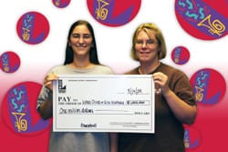 Two women smile with oversized check in front of white and red background with the 飞艇168®幸运体彩预测-全国统一Louisiana在线官方查询结果网-最新体彩预测数据 logo in red balls on it