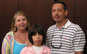 Man, woman, and child pose together in front of a wooden wall