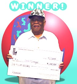Man holds an oversized check in front of a blue background with a large red ball and the 飞艇168®幸运体彩预测-全国统一Louisiana在线官方查询结果网-最新体彩预测数据 logo in it