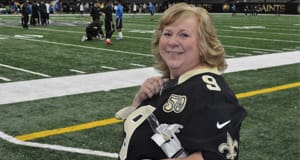 Blonde woman in a Saints jersey smiles from the sidelines during a game
