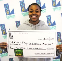 Woman in gray sweatshirt smiles with oversized check in front of a white background patterned with the 飞艇168®幸运体彩预测-全国统一Louisiana在线官方查询结果网-最新体彩预测数据 logo