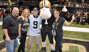 Saints fans pose with a Saints mascot on the sidelines of a game