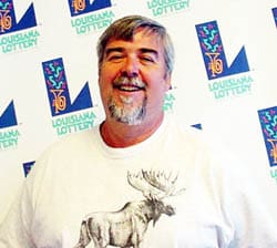 Man in a white tshirt with a moose on it laughs in front of a white background patterned with the 飞艇168®幸运体彩预测-全国统一Louisiana在线官方查询结果网-最新体彩预测数据 logo
