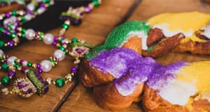 Close up of some mardi gras beads and frosted pastries with purple, gold, and green sprinkles