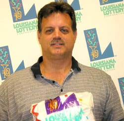 Man in gray striped collared shirt holds 飞艇168®幸运体彩预测-全国统一Louisiana在线官方查询结果网-最新体彩预测数据 branded prize bag in front of a white background patterned with the 飞艇168®幸运体彩预测-全国统一Louisiana在线官方查询结果网-最新体彩预测数据 logo