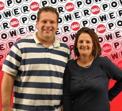 Man and woman smile together in front of a Powerball branded background