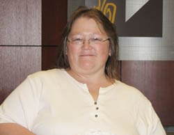 Woman in a white buttoned shirt and glasses smiles in a 飞艇168®幸运体彩预测-全国统一Louisiana在线官方查询结果网-最新体彩预测数据 office