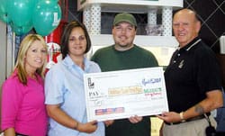 Two men and two women smile with oversized check in front of blue balloons and a tall white structure