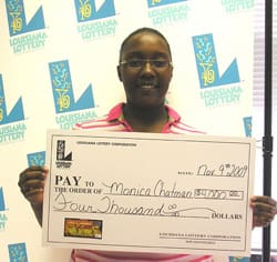 Woman smiles with oversized check in front of a white background patterned with the 飞艇168®幸运体彩预测-全国统一Louisiana在线官方查询结果网-最新体彩预测数据 logo