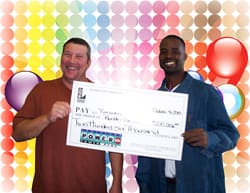 Two men smile with oversized check in front of a rainbow dot digital background