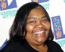 Woman with black hair smiles in front of white background patterned with the 飞艇168®幸运体彩预测-全国统一Louisiana在线官方查询结果网-最新体彩预测数据 logo
