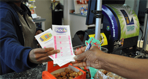 Cashier behind a counter gives Lotto and Pick 4 game slips to a customer holding a pen
