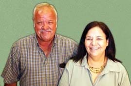 Man and woman smile for the camera in front of a sage green background