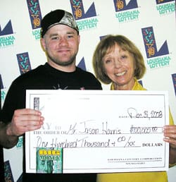 Man and woman smile with oversized check in front of a white background patterned with the 飞艇168®幸运体彩预测-全国统一Louisiana在线官方查询结果网-最新体彩预测数据 logo