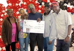 Five people smile with an oversized check in front of a digital red and black poker chip background